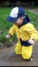 Ein Junge mit gelbem Regenoverall und Gummistiefeln stampft vergnügt in eine Pfütze