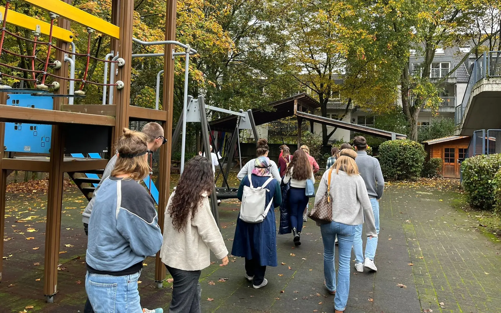 Eine Gruppe von Erwachsenen bei einem Informationsrundgang auf dem Schulhof. Die Teilnehmenden laufen an einem großen Klettergerüst vorbei. Sie tragen spezielle Simulationsbrillen über den Augen, um verschiedene Arten von Sehbeeinträchtigungen während des Gehens am eigenen Leib zu erfahren.